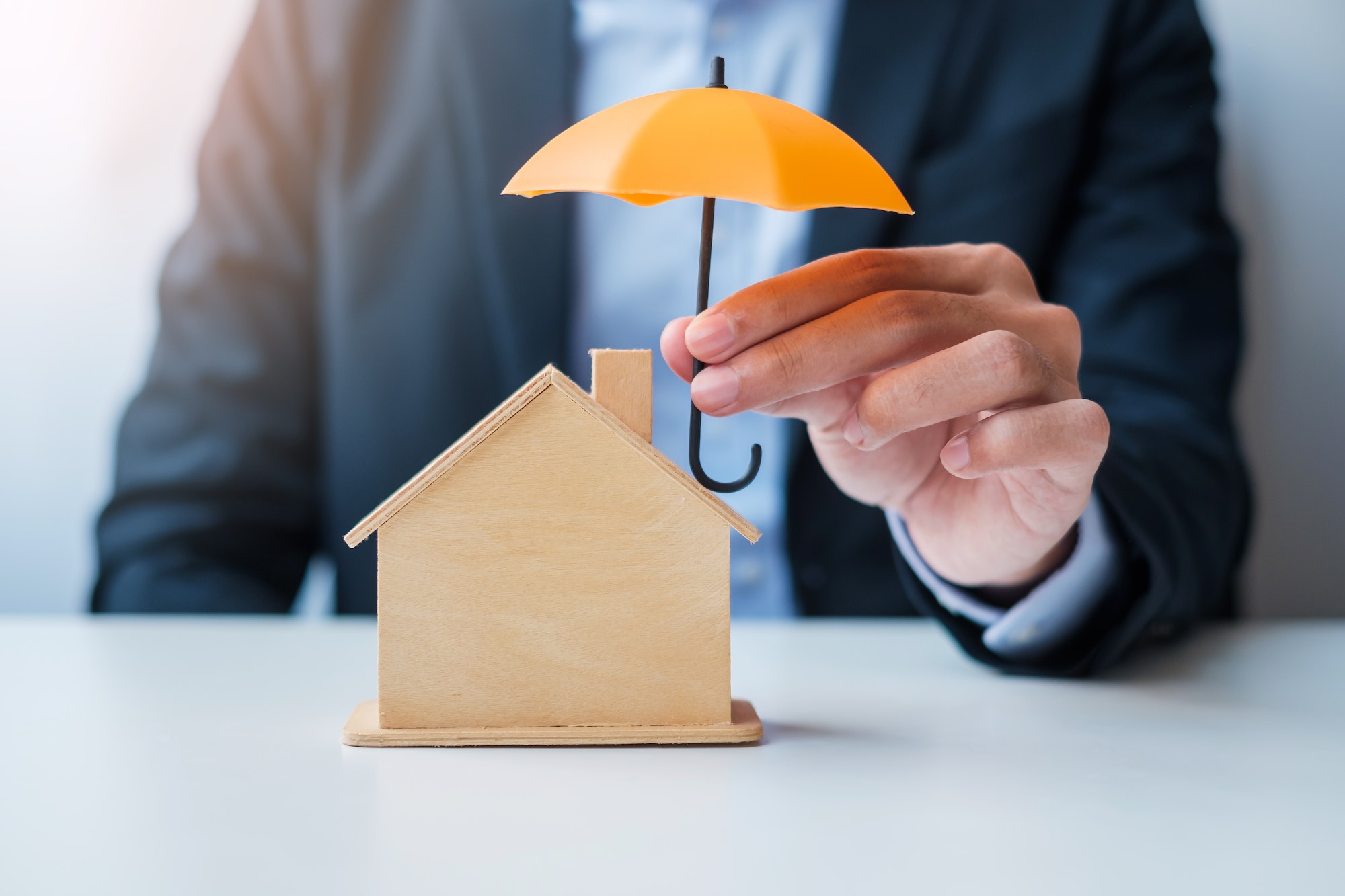 Businessman hand holding orange Umbrella cover wooden Home model. real estate, insurance and propert